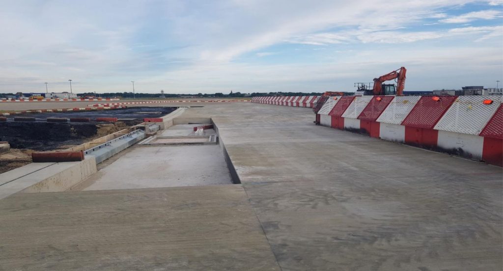 Completed concrete apron bays behind safety barriers at Gatwick Airport