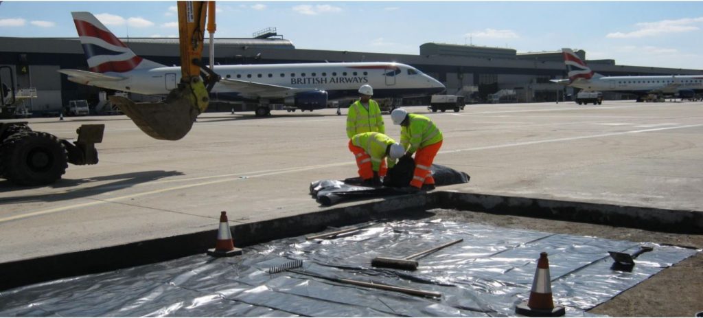 TAG team laying membrane in a concrete bay beside a parked aircraft at London City Airport