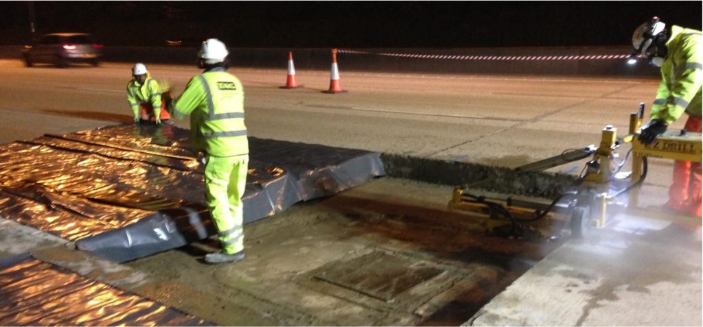 Crew cutting out a damaged concrete bay around a manhole on the M25 at night