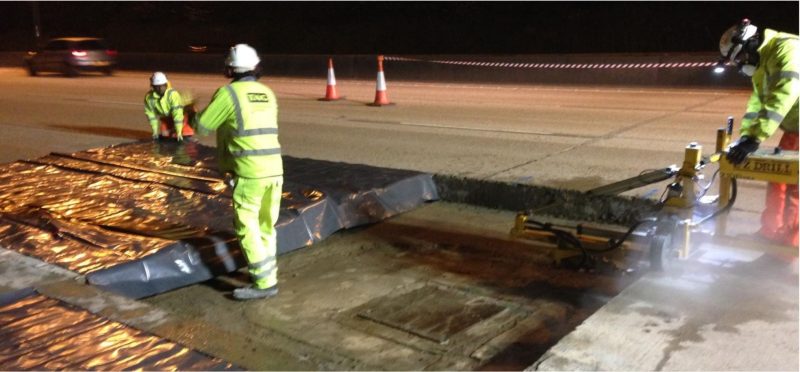 Crew cutting out a damaged concrete bay around a manhole on the M25 at night